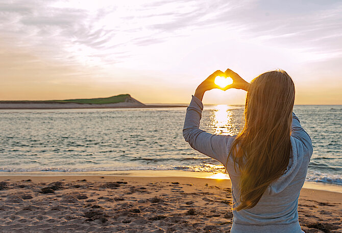 eine Frau blickt am Strand in den Sonnenuntergang
